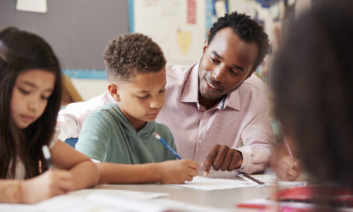 A teacher working with elementary school boy at his desk